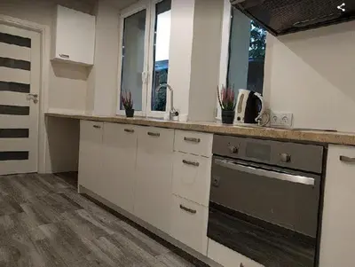 a kitchen with white cabinets and a sink and two windows at OldKrak Apartment in Kraków