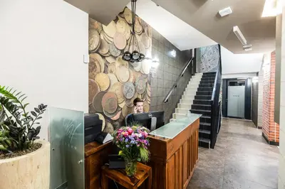 a woman sitting at a desk in a lobby with a wall of logs at Hotel Perfect in Kraków