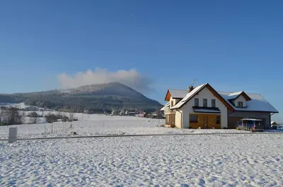 a house in the snow with a mountain in the background at Pokoje na Wzgórzu in Kasina Wielka