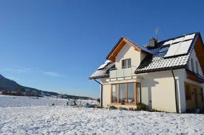 a house with snow on its roof on a snowy field at Pokoje na Wzgórzu in Kasina Wielka