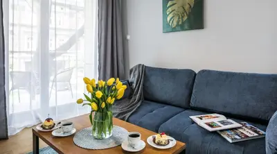 a living room with a blue couch and a table with yellow flowers at Vistula Boutique Exclusive Apartments in Kraków