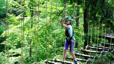 a boy standing on a suspension bridge in the forest at Pokoje w Oberży Czarny Groń in Rzyki