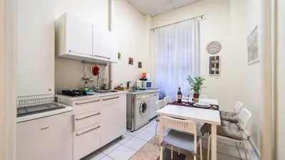 a kitchen with white cabinets and a table and a table and chairs at Fogra Travel Apartment in Kraków