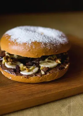 a doughnut sandwich with powdered sugar on a cutting board at Draggo House Rooms - Old Town in Kraków