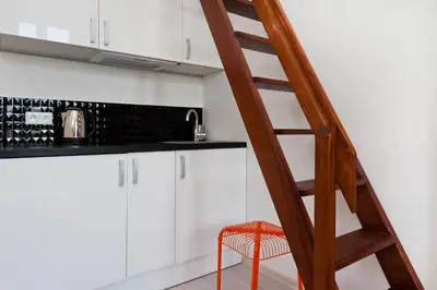 a staircase in a kitchen with white cabinets and a red stool at Dietla 99 - Studio by Homeprime in Kraków