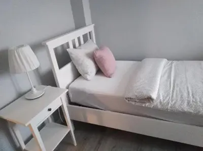 a white bed with a pink pillow and a night stand at Apartament Julek klimatyzowany in Oświęcim