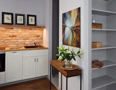 a kitchen with white cabinets and a painting on the wall at Wawrzyńca Brick Apartment Kazimierz in Kraków