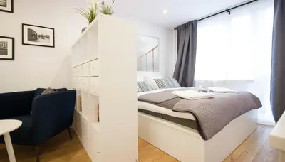 a small white bedroom with a bed and a chair at Rakowicka Apartament in Kraków