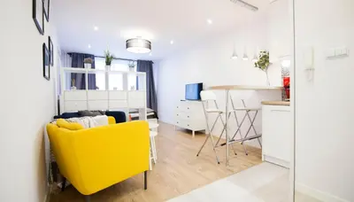 a living room with a yellow chair and a kitchen at Rakowicka Apartament in Kraków