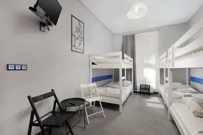 a room with white bunk beds and a table and chairs at Moon Hostel Kraków in Kraków
