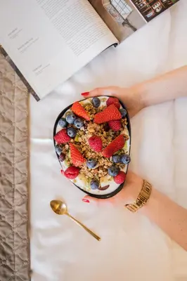 a bowl of cereal and fruit on a table with a book at Balthazar Design Hotel in Kraków