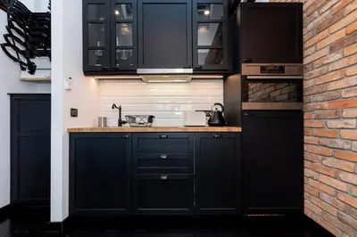 a kitchen with black cabinets and a brick wall at Apartments Starowislna Kazimierz Cracow by Noclegi Renters in Kraków