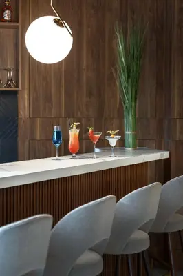 a bar with four drinks on a counter with chairs at Metropolo by Golden Tulip Krakow in Kraków
