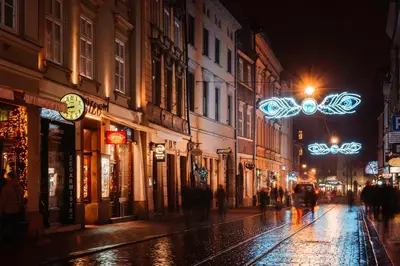 a wet city street at night with lights at The Angels Apartments Krakow Old Town in Kraków