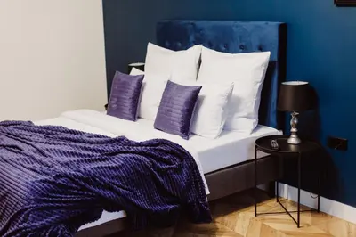 a bed with purple and white pillows and a blue wall at Kings City - Blich Apartment in Kraków