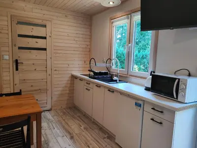 a kitchen with white cabinets and a microwave and a table at Domki Całoroczne - Tarlagowy Bór in Bebło