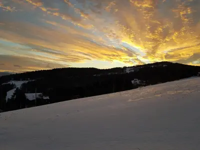 a sunset on a snow covered slope with the sun setting at Bacówka na Zadzielu in Laskowa