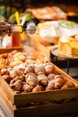 a person is sprinkling powdered sugar on a tray of doughnuts at Park Inn by Radisson Krakow in Kraków