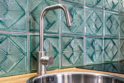 a sink in a kitchen with a green tiled wall at Relaks Apartamenty in Kraków