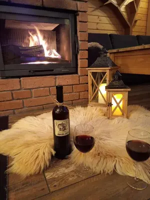 a bottle of wine and two glasses on a fur rug with a fireplace at Stodoła Simonka na punkcie widokowym in Zawoja