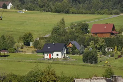a white house with a red door in a green field at Domek Tadeusz in Śleszowice Górne