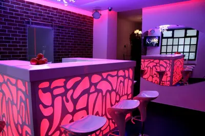 a bar with pink lighting and stools in a room at Greg&Tom Party Hostel in Kraków