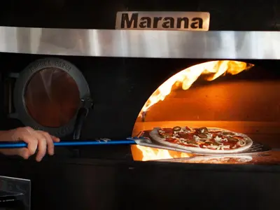 a person is cooking two pizzas in an oven at The Loft Hotel Adults Only in Kraków