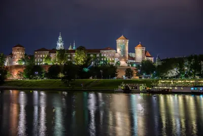 a large building in front of a river at night at Art Apartment in Kraków