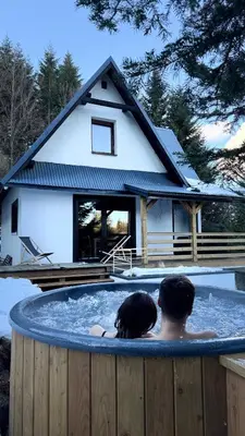 a man and woman sitting in a hot tub in front of a house at Mountain Cottage Lubomierz in Lubomierz