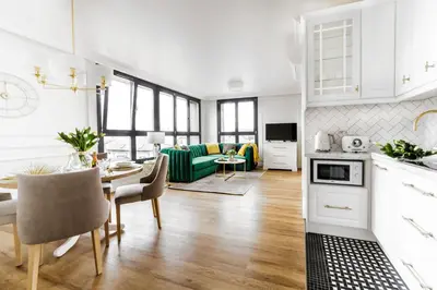 a kitchen and living room with white cabinets and a table at Apartament Golden Place 2 in Kraków