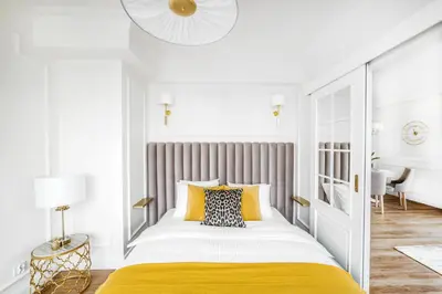 a white bedroom with a large bed with yellow sheets at Apartament Golden Place 2 in Kraków