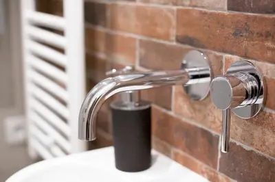 a bathroom sink with a faucet next to a brick wall at D&A Apartmetns Lenartowicza in Kraków
