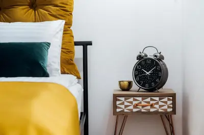 a clock on a night stand next to a bed at Tomasza 20 Apartments in Kraków