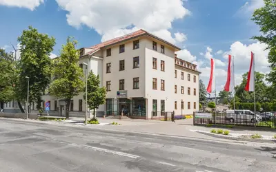 a white building with red flags in front of it at Domus Mater Hotel in Kraków