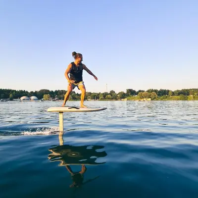 a woman standing on a surfboard in the water at Costa del Kryspi Całoroczne Domy na Wodzie in Cholerzyn