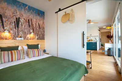 a bedroom with a green bed and a kitchen at Costa del Kryspi Całoroczne Domy na Wodzie in Cholerzyn
