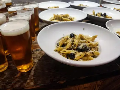 a table with plates of food and glasses of beer at Greg&Tom Beer House Hostel in Kraków