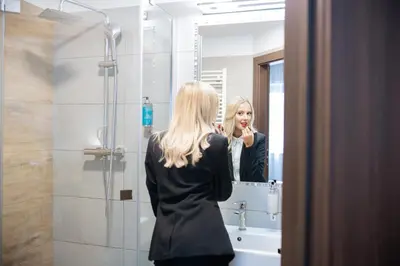 a woman brushing her teeth in front of a mirror at Hotel CONRAD Comfort in Kraków