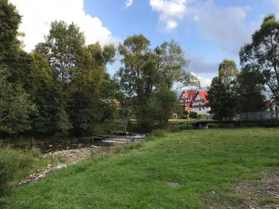 a river in a field with a house in the background at Osada Babiogórska - domki gościnne in Zawoja