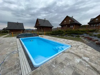 a large swimming pool on a patio with houses at Domki Zagroda Domek z bala z basenem & sauna & balia z hydromasażem in Słopnice