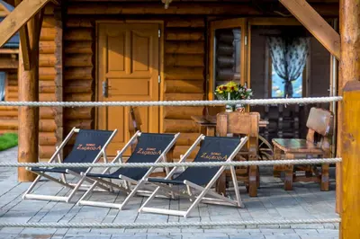 two deckchairs and a table and chairs in front of a cabin at Domki Zagroda Domek z bala z basenem & sauna & balia z hydromasażem in Słopnice