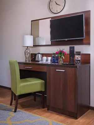 a desk with a green chair and a clock on a wall at Aparthotel Lumen in Kraków