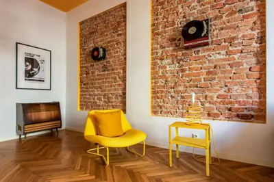 a living room with a yellow chair and a brick wall at City Vibes Apartments in Kraków