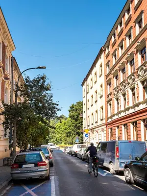 a person riding a bike down a street with parked cars at Green view apartment / Kochanowskiego in Kraków