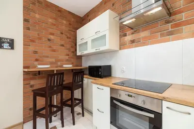 a kitchen with white cabinets and a brick wall at Deluxe Apartments Kraków Brzozowa by Noclegi Renters in Kraków