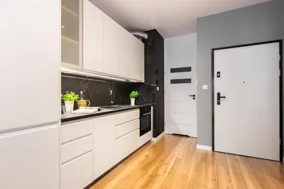 a kitchen with white cabinets and a wooden floor at NOVUM Apartment with Parking in Kraków