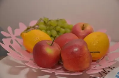 a pink bowl of fruit with apples oranges and grapes at Apartament Skałka in Jaworzno