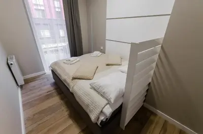 a small bedroom with a bed and a large window at Krakowiak Apartments in Kraków
