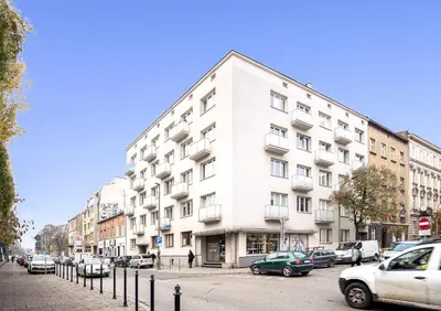 a white building on a city street with parked cars at Polka Apartment 2-bed in Kraków