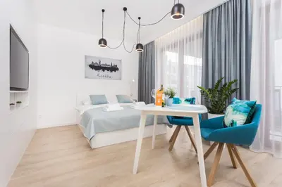 a white bedroom with a bed and a table and a blue chair at City of the Kings - Smile Apartment in Kraków